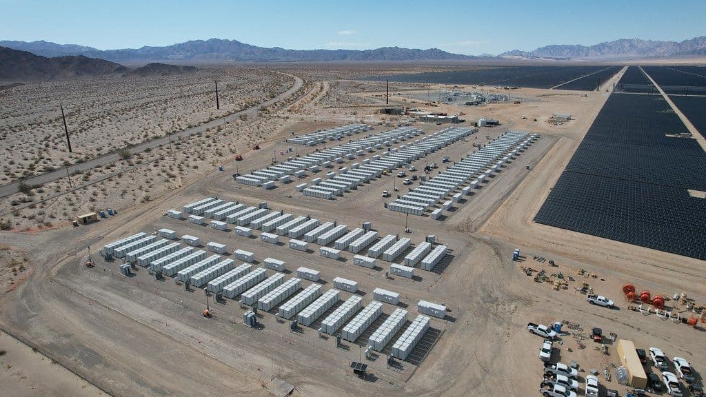 Rows of battery storage containers beside a large solar farm in the desert